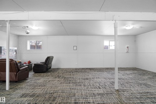 Spacious lower level featuring patterned carpet flooring, two windows, recessed lighting, and white support columns - 4816 155 Ave, Edmonton, AB 