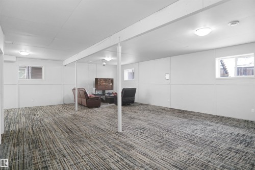 Spacious finished room featuring patterned carpet flooring, white paneled walls, multiple windows, and ceiling-mounted light fixtures - 4816 155 Ave, Edmonton, AB 