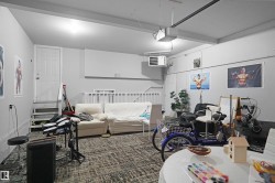 Spacious garage featuring light gray walls, textured carpeting, overhead lighting, and a white access door with stairs - 