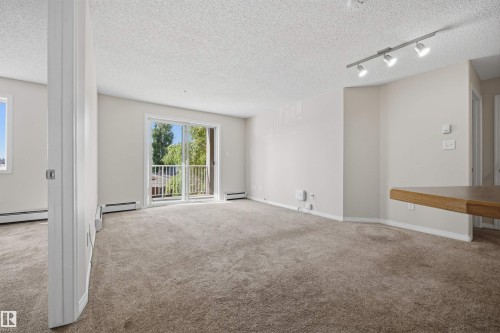 Living area featuring neutral-tone carpeting, light-colored walls, and a sliding glass door opening to a balcony - 201 3425 19 Street Nw, Edmonton, AB 
