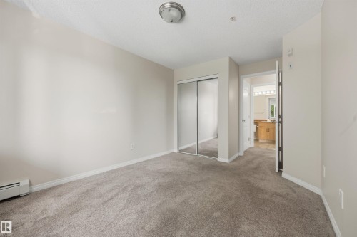 The second bedroom features a mirrored closet, baseboard heating, and a ceiling light fixture. - 201 3425 19 Street Nw, Edmonton, AB 