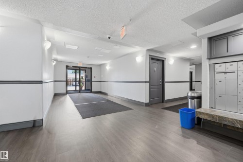 Building entry featuring glass double doors, wood-finish flooring, two-tone wall paneling, and wall-mounted light fixtures - 201 3425 19 Street Nw, Edmonton, AB 