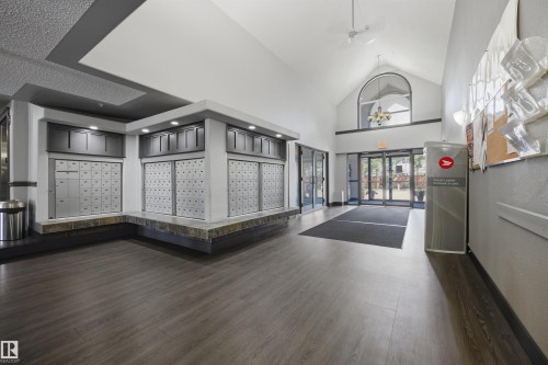 Spacious lobby featuring wood-finish flooring, a vaulted ceiling with an arched window, and built-in mailboxes with overhead lighting - 201 3425 19 Street Nw, Edmonton, AB 