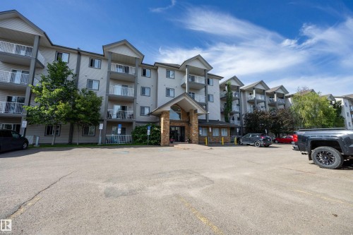 Multi-story building featuring individual balconies with white railings, a stone-clad entrance, and a paved parking area - 201 3425 19 Street Nw, Edmonton, AB 