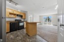 Open-concept kitchen featuring wood cabinetry, black appliances, track lighting, and a central island - 201 3425 19 Street Nw, Edmonton, AB 