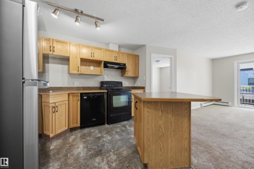 Kitchen featuring wood cabinetry, dark countertops, and black appliances - 201 3425 19 Street Nw, Edmonton, AB 