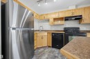 Kitchen featuring wood-finish cabinetry, stainless steel top-freezer refrigerator, black electric range, black built-in dishwasher, and a stainless steel sink with a high-arch faucet - #201 3425 19 St Nw Nw, Edmonton, AB 