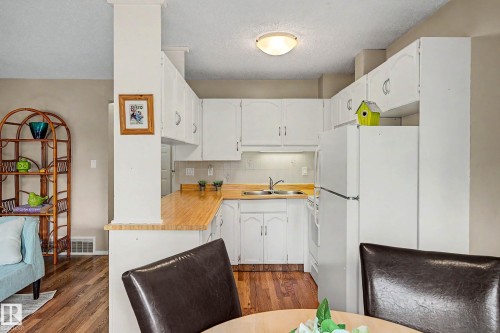 U-shaped kitchen featuring white cabinetry, light wood-finish countertops, and white appliances - 19 Pineview Drive, St. Albert, AB 