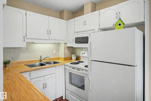 Kitchen featuring white cabinetry, wood-finish countertops, a double basin stainless steel sink, tile backsplash, and white appliances including a refrigerator, range, and microwave - 19 Pineview Drive, St. Albert, AB 