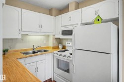 Kitchen featuring white cabinetry, wood-finish countertops, a double basin stainless steel sink, tile backsplash, and white appliances including a refrigerator, range, and microwave - 