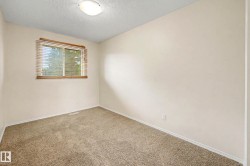 Carpeted room featuring a window with horizontal blinds and a wood-finish frame, light-toned walls, and a flush-mount ceiling light fixture - 