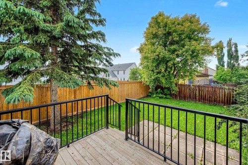 Private backyard featuring a wooden deck with black metal railings, a manicured lawn, concrete patio area, and mature trees - 19 Pineview Drive, St. Albert, AB 