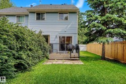 Rear exterior featuring light blue horizontal siding, a wooden deck with black metal railings, a sliding glass door, and a grass lawn - 