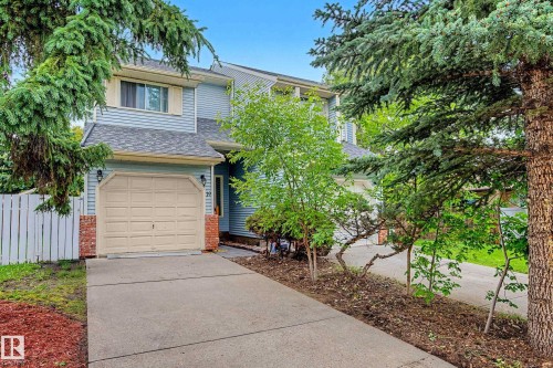 Two-story residence featuring light blue siding, a two-car garage with a panel door, and red brick accents - 19 Pineview Drive, St. Albert, AB 