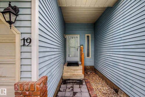 Entryway featuring light blue siding, a white front door with glass panels, concrete steps, a narrow vertical window, and a wood handrail - 19 Pineview Drive, St. Albert, AB 