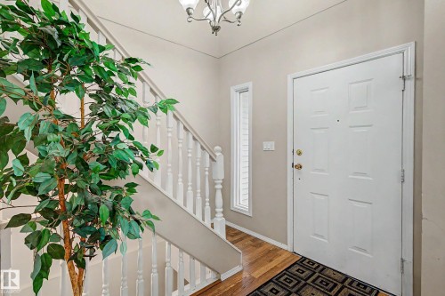 Entryway featuring a paneled door with brass hardware, wood-finish flooring, a sidelight window, and a white spindle staircase - 19 Pineview Drive, St. Albert, AB 