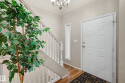 Entryway featuring a paneled door with brass hardware, wood-finish flooring, a sidelight window, and a white spindle staircase - 