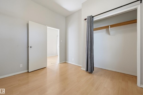 Bright room featuring wood-finish flooring, light gray wall paint, white trim, and a functional closet with a hanging rod and shelf - 11450 71 Street Nw, Edmonton, AB 