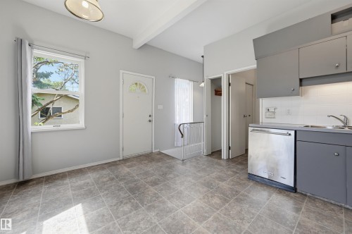 Kitchenette and dining area featuring tiled flooring, a stainless steel dishwasher, grey cabinetry, a white subway tile backsplash, and an entry door with a decorative glass insert - 11450 71 Street Nw, Edmonton, AB 