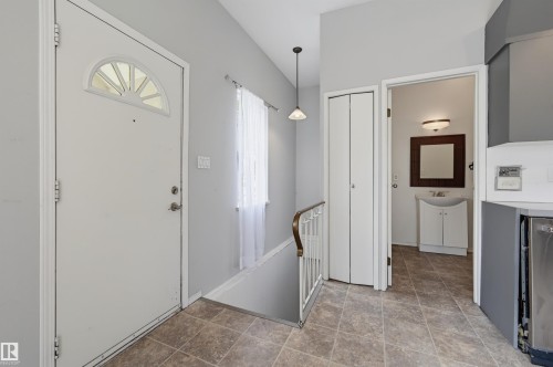 Entryway featuring neutral wall colors, tile flooring, a white paneled door with an arched window, and a white balustrade leading to a lower level - 11450 71 Street Nw, Edmonton, AB 