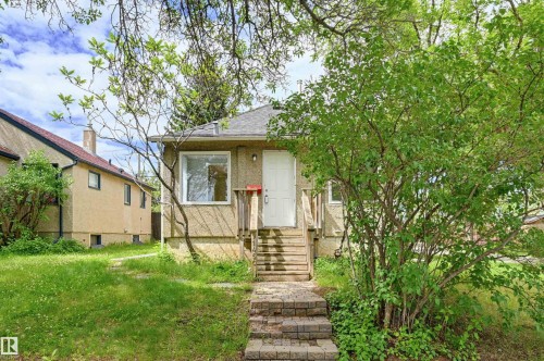 Single-story stucco residence featuring a white entry door, exterior wooden stairs, and a paver stone walkway - 11450 71 Street Nw, Edmonton, AB 
