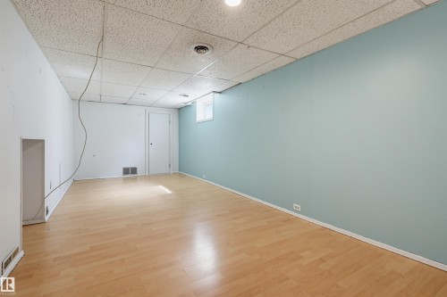 Spacious room featuring wood-finish flooring, a drop ceiling, and a light blue accent wall - 11450 71 Street Nw, Edmonton, AB 