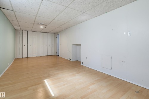 Spacious room featuring light wood-finish flooring, acoustic tile ceiling, and multiple bifold closet doors - 11450 71 Street Nw, Edmonton, AB 