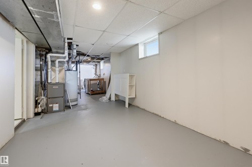 Unfinished basement area featuring a utility furnace and water heater, exposed ductwork, a drop ceiling, and a high-set window - 11450 71 Street Nw, Edmonton, AB 