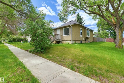 Single-story residence featuring a stucco exterior, a dark shingled roof, multiple windows, and a wood deck with stairs - 11450 71 Street Nw, Edmonton, AB 