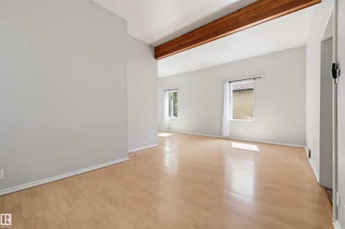 Open-concept living space with exposed wood ceiling beams, light wood-finish flooring, multiple windows, and a neutral wall palette - 11450 71 Street Nw, Edmonton, AB 