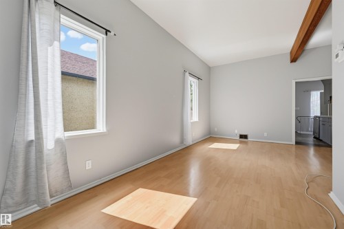 Spacious room featuring wood-finish flooring, light grey walls, and a vaulted ceiling with an exposed wood beam - 11450 71 Street Nw, Edmonton, AB 