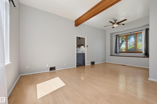Spacious interior area featuring wood-finish flooring, a vaulted ceiling with exposed wood beams, and a modern ceiling fan - 11450 71 Street Nw, Edmonton, AB 