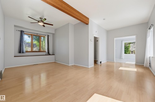 Expansive room featuring light wood-finish flooring, a prominent wooden ceiling beam, and a ceiling fan with light fixture - 11450 71 Street Nw, Edmonton, AB 