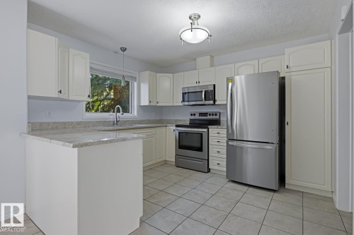 Contemporary kitchen featuring white cabinetry, light-toned countertops, stainless steel appliances, and tiled flooring - 6 1237 Carter Crest Road, Edmonton, AB 
