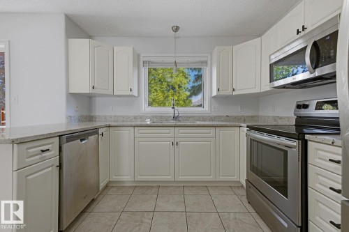 Kitchen featuring white cabinetry, light-toned countertops, a stainless steel dishwasher, a stainless steel range with an overhead microwave, and neutral-toned tiled flooring - 6 1237 Carter Crest Road, Edmonton, AB 