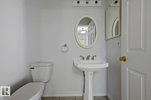 Pedestal sink with brass-finish faucet, oval framed mirror, and panel door with brass-finish hardware - 6 1237 Carter Crest Road, Edmonton, AB 