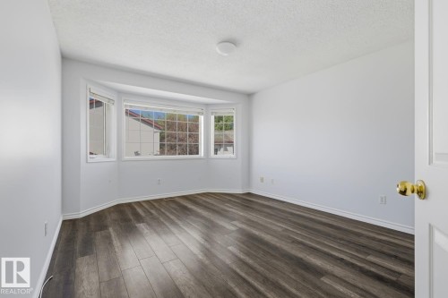 Spacious room featuring a bay window, wood-finish flooring, white baseboards, and a neutral wall color - 6 1237 Carter Crest Road, Edmonton, AB 