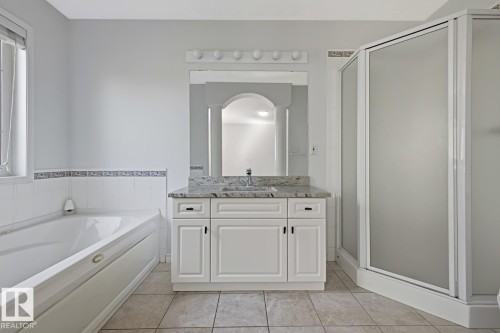 Bathroom featuring a white vanity with a light-toned countertop, a built-in tub, a frosted glass shower enclosure, and tiled flooring - 6 1237 Carter Crest Road, Edmonton, AB 