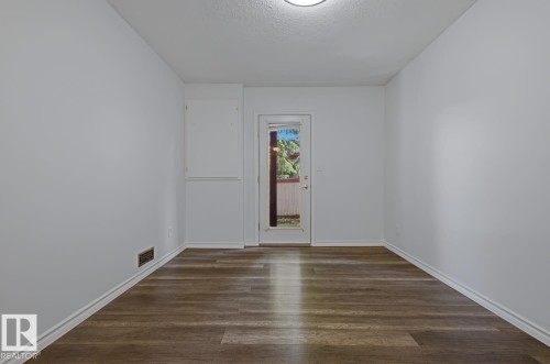 Spacious room featuring wood-finish flooring, white baseboards, and a glass-paneled exterior door - 6 1237 Carter Crest Road, Edmonton, AB 