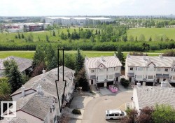 Townhome exterior featuring light-colored siding, a grey shingled roof, and a mature tree line backdrop - 