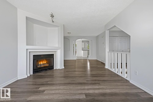 Spacious room featuring wood-finish flooring and a central fireplace with a light-toned surround - 6 1237 Carter Crest Road, Edmonton, AB 