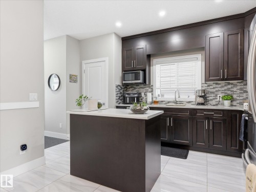 Contemporary kitchen featuring rich wood-finish cabinetry, light-toned countertops, a mosaic tile backsplash, and stainless steel appliances - 12820 68 Street, Edmonton, AB - Indoor Photo Showing Kitchen