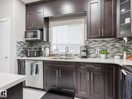 Modern kitchen featuring dark wood-finish cabinetry, light stone-finish countertops, and a mosaic tile backsplash - 12820 68 Street, Edmonton, AB - Indoor Photo Showing Kitchen With Double Sink With Upgraded Kitchen