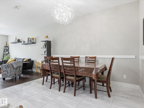 Dining area featuring a contemporary chandelier, light gray walls, and white tile flooring - 12820 68 Street, Edmonton, AB - Indoor Photo Showing Dining Room