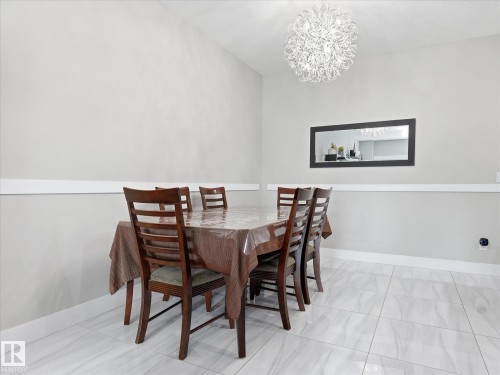 Spacious dining area featuring a contemporary chandelier, light gray walls, white chair rail molding, and large format white tile flooring - 12820 68 Street, Edmonton, AB - Indoor Photo Showing Dining Room