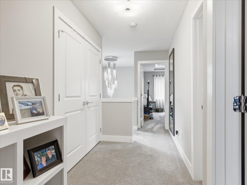 Carpeted hallway featuring a contemporary chandelier, recessed ceiling lighting, white interior doors, and a built-in shelving unit - 12820 68 Street, Edmonton, AB - Indoor Photo Showing Other Room
