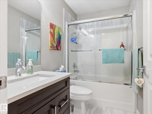 Bathroom featuring a dark wood-finish vanity with a light countertop and an integrated sink, a mirrored wall, a toilet, a tub with a sliding glass door enclosure, and light-toned flooring - 12820 68 Street, Edmonton, AB - Indoor Photo Showing Bathroom