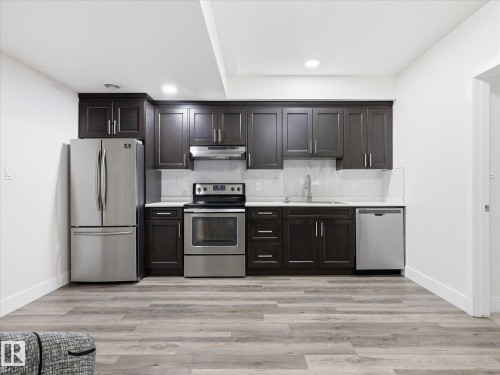 Contemporary kitchen featuring dark wood cabinetry, stainless steel appliances, white countertops, and a full tile backsplash - 12820 68 Street, Edmonton, AB - Indoor Photo Showing Kitchen