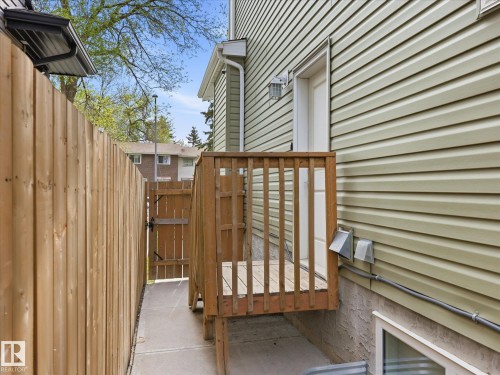 Wood privacy fence defining the property line, concrete pathway, and an exterior door with a wood deck entry - 12820 68 Street, Edmonton, AB - Outdoor With Exterior