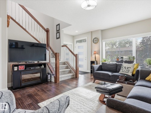 Expansive living area featuring rich wood-finish flooring, a two-story staircase with wood railings and metal balusters, and large windows with horizontal blinds - 12820 68 Street, Edmonton, AB - Indoor Photo Showing Living Room